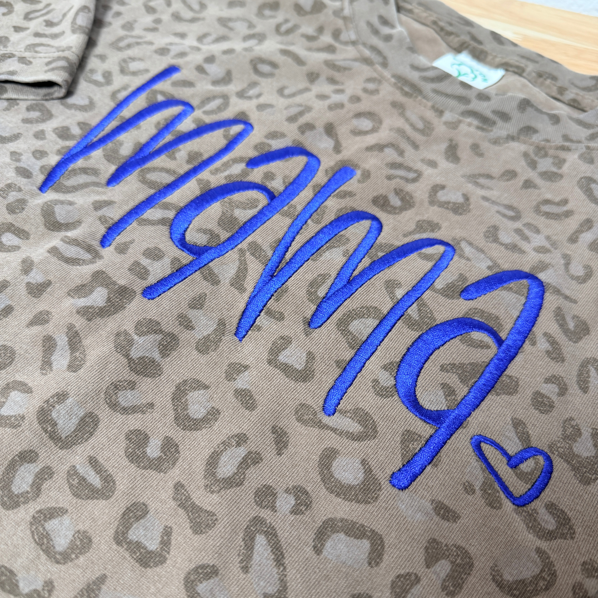 Leopard print fabric with blue embroidered text and heart symbol