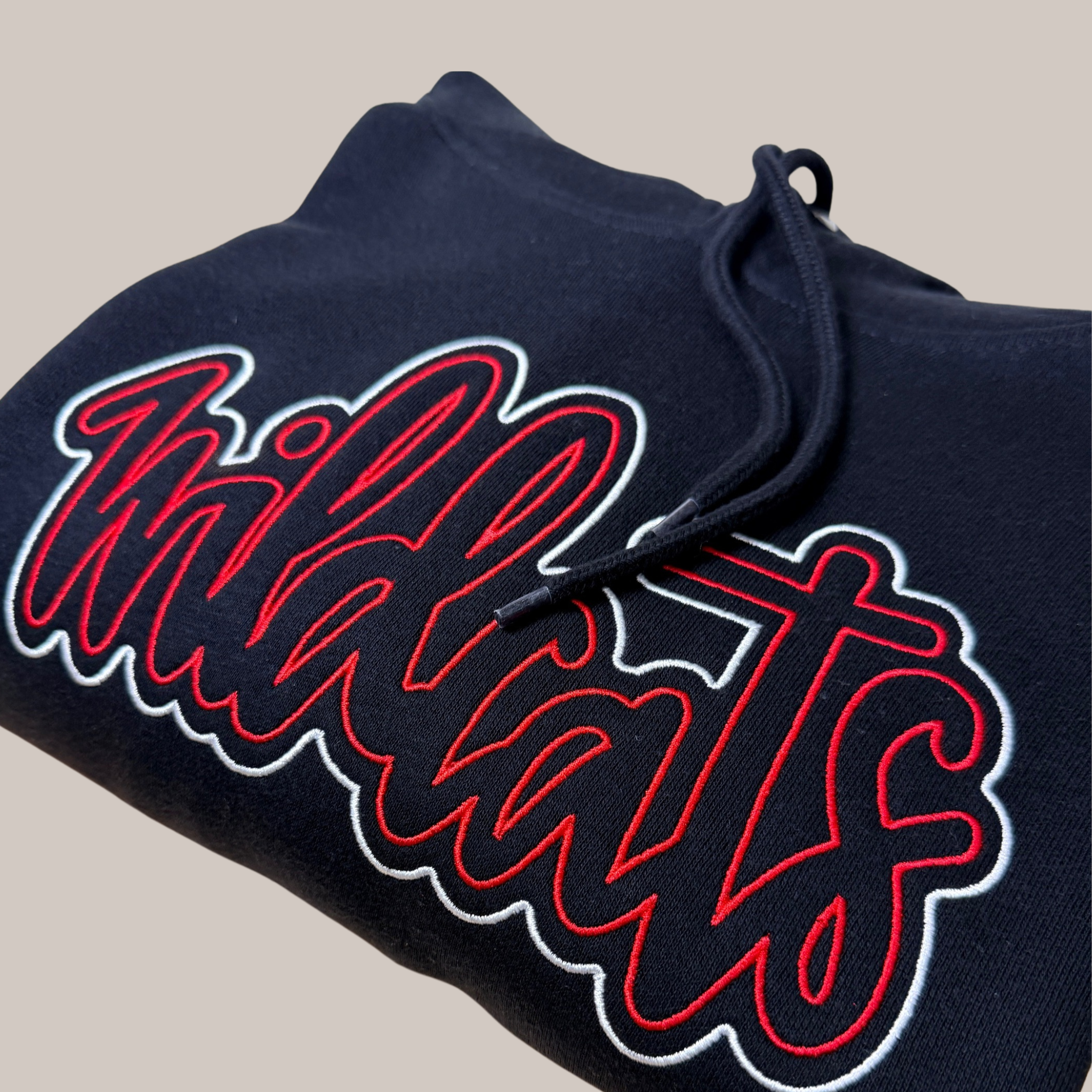 Embroidered Wildcats script hoodie in red and white thread on a dark fleece sweatshirt, close-up detail