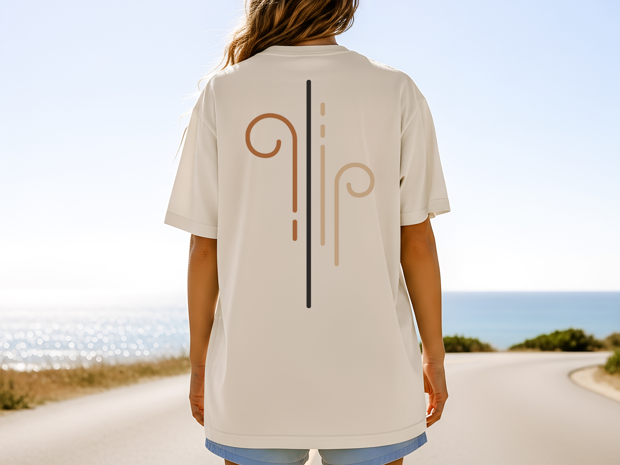 Person wearing a beige t-shirt with a logo on the back, standing on a road with a scenic view.