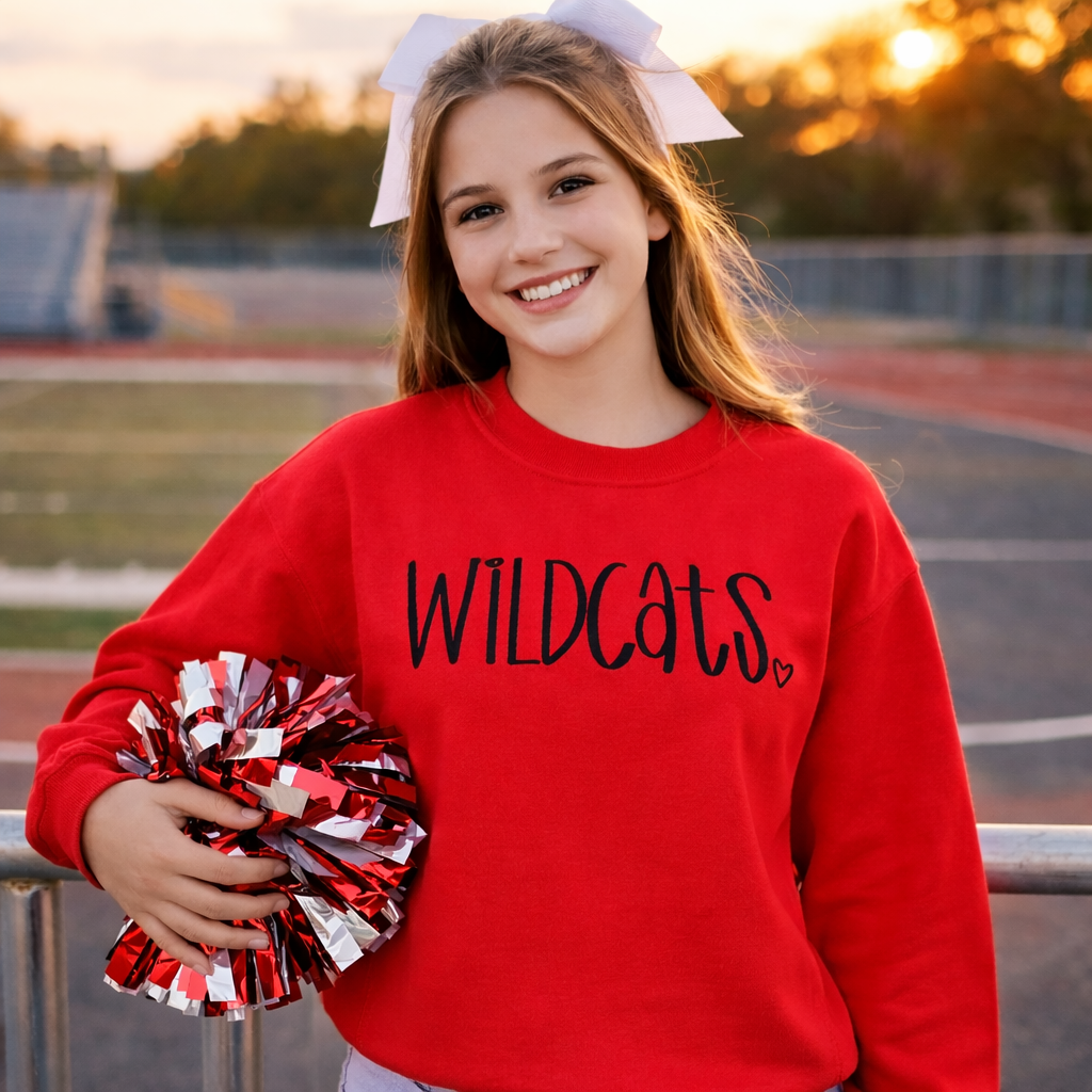 Girl in red 'Wildcats' sweatshirt with pom-poms on a sports field