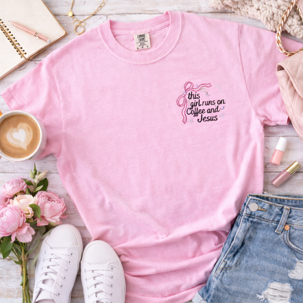 Pink t-shirt with text on a table with flowers, shoes, and accessories