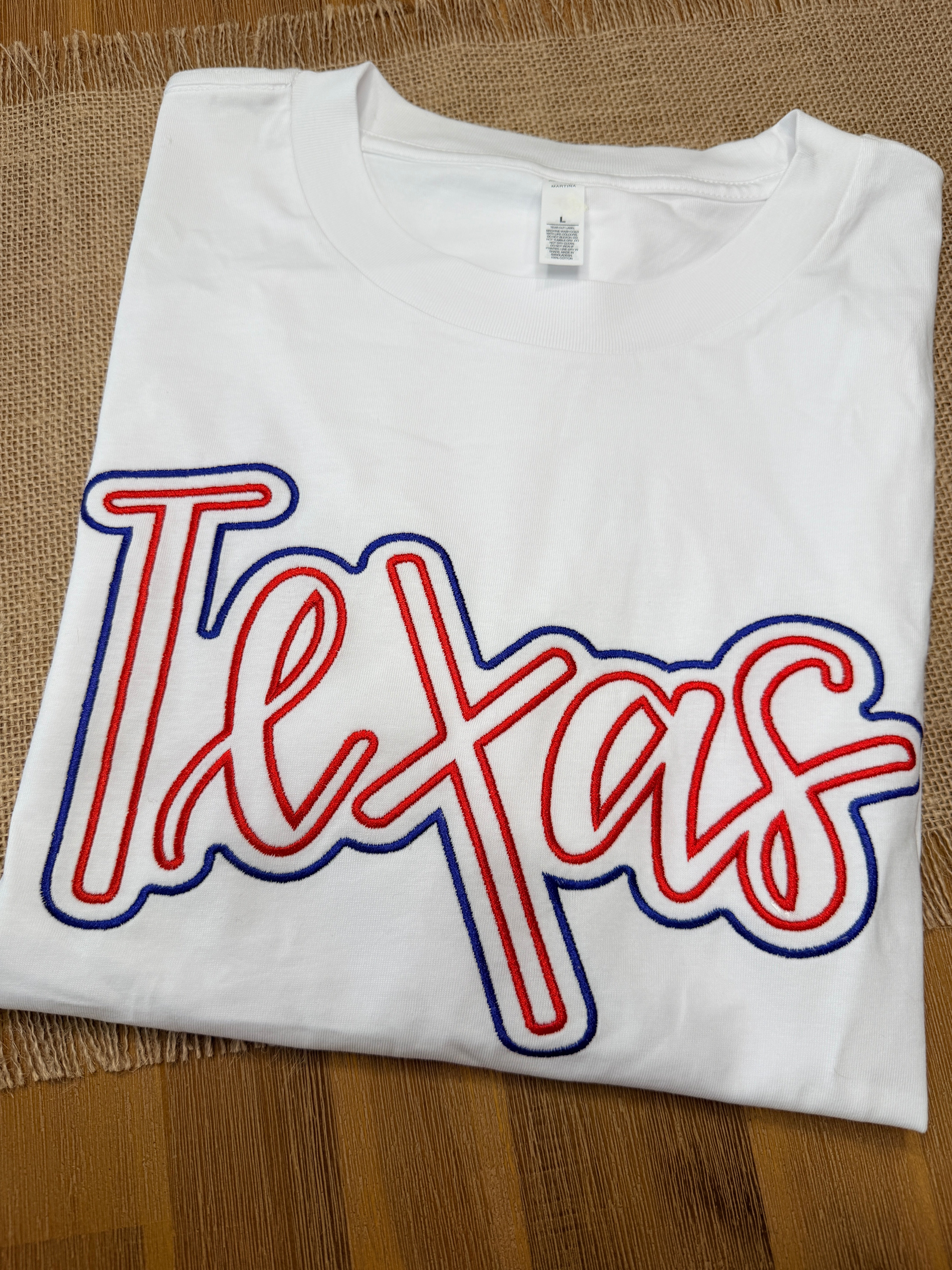 White sleeveless shirt with red and blue 'Tex' logo on a wooden surface
