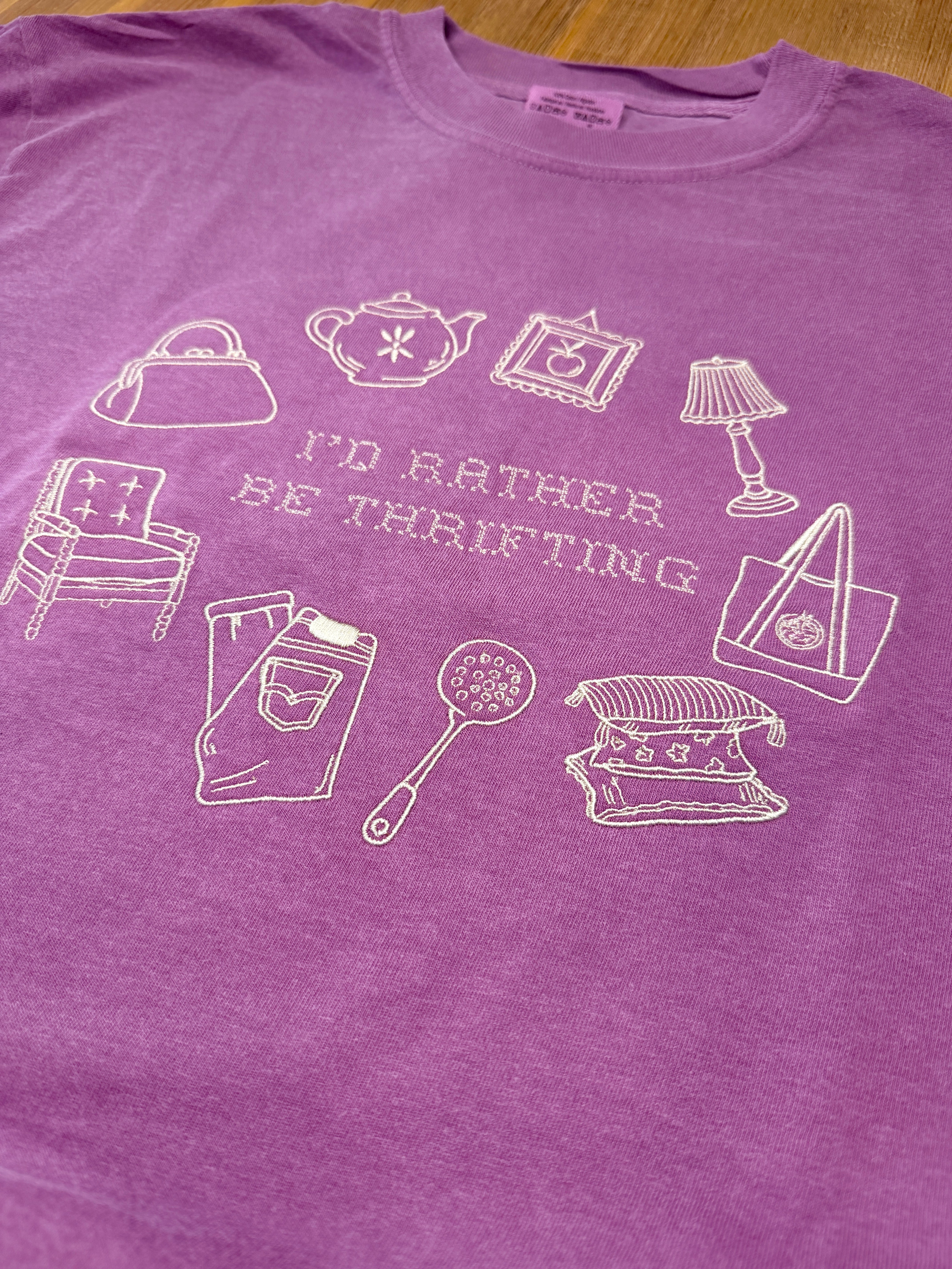 Purple tank top with white graphic designs and text on a wooden surface