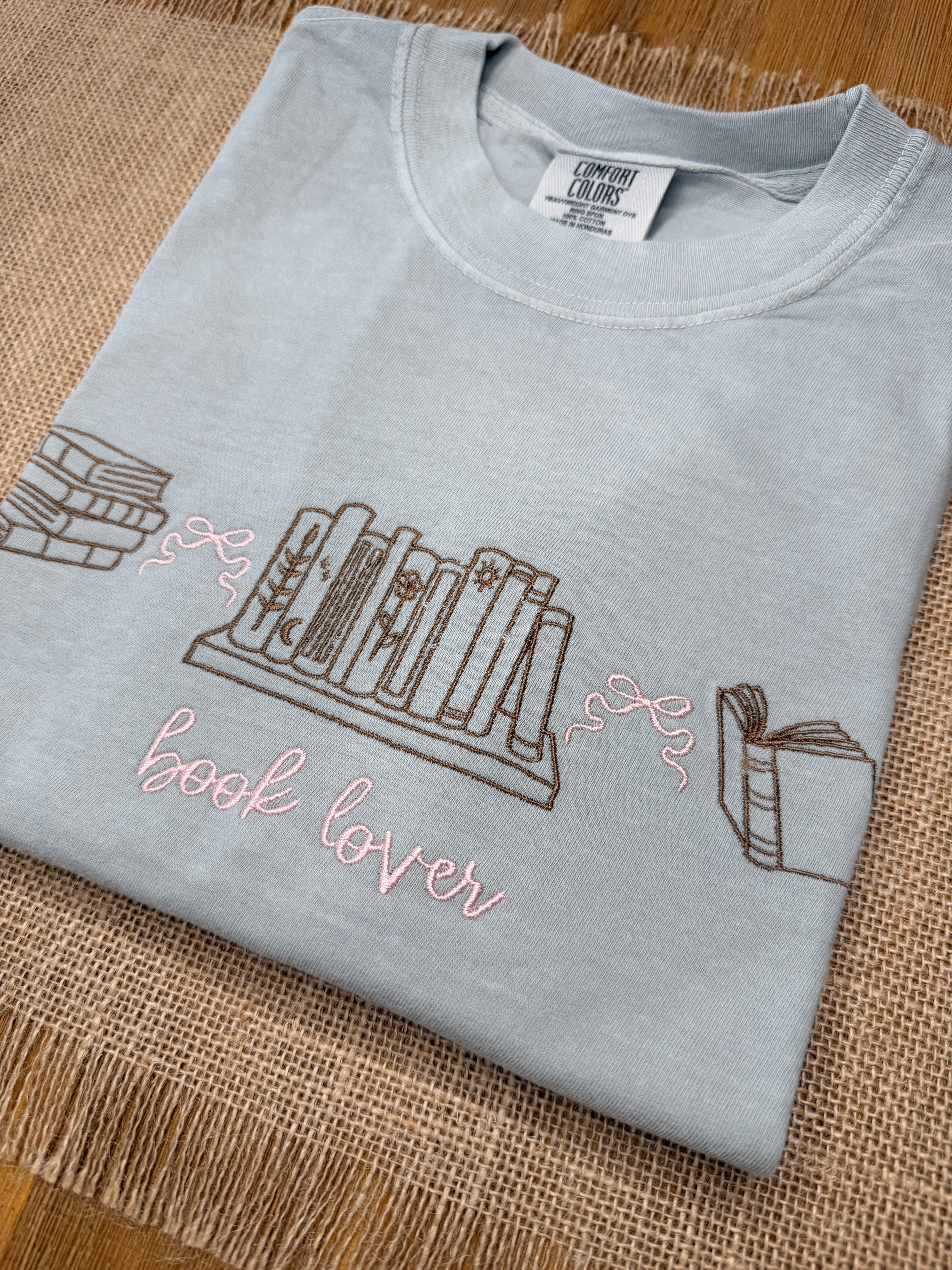 Gray t-shirt with book-themed design on a textured surface
