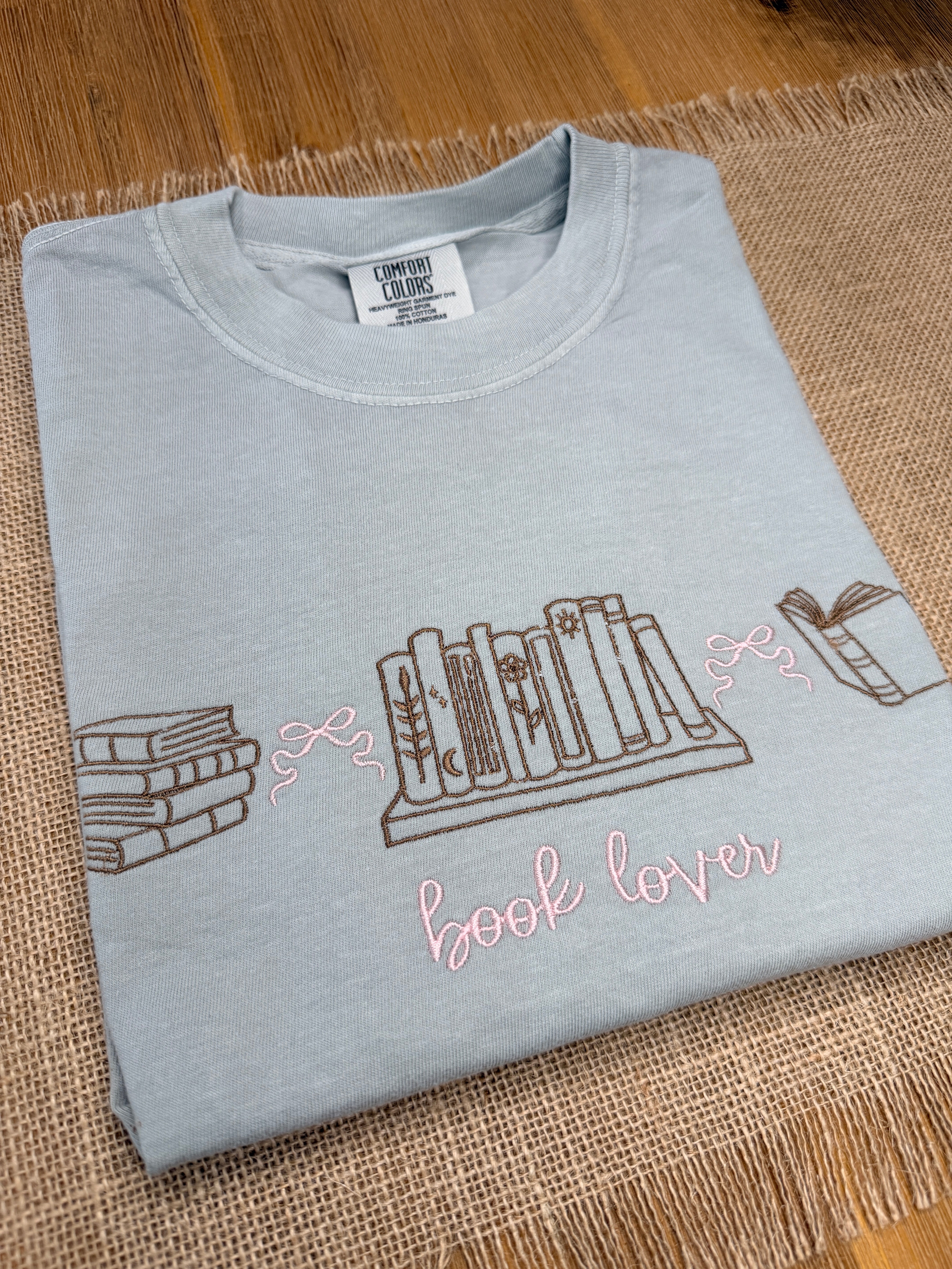 Light blue t-shirt with book-themed design on a textured surface