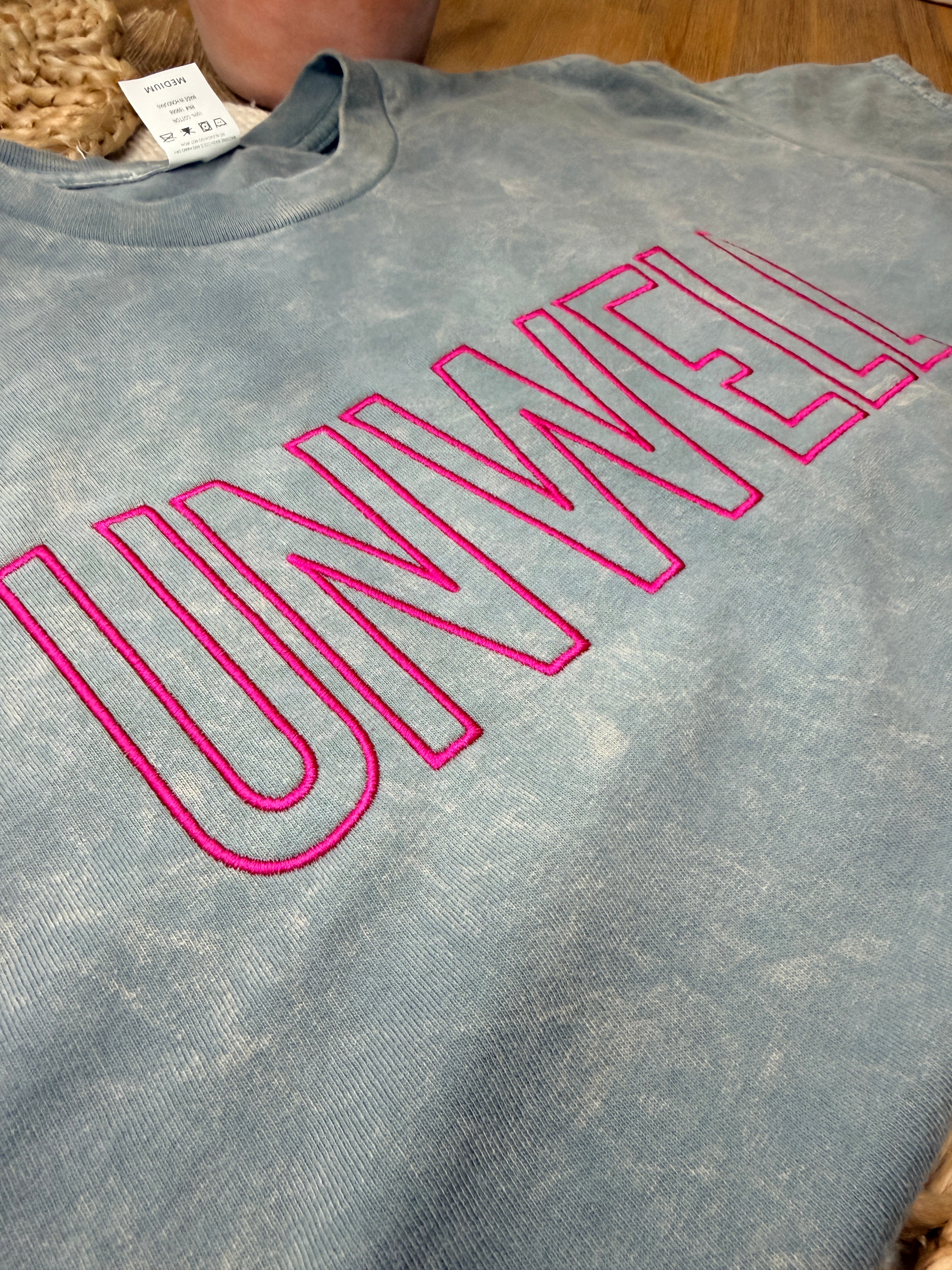 Gray acid-washed Cotton Collective tour tee with bold pink “UNWELL” embroidery across the chest. Relaxed fit with soft vintage wash and minimalist statement design.