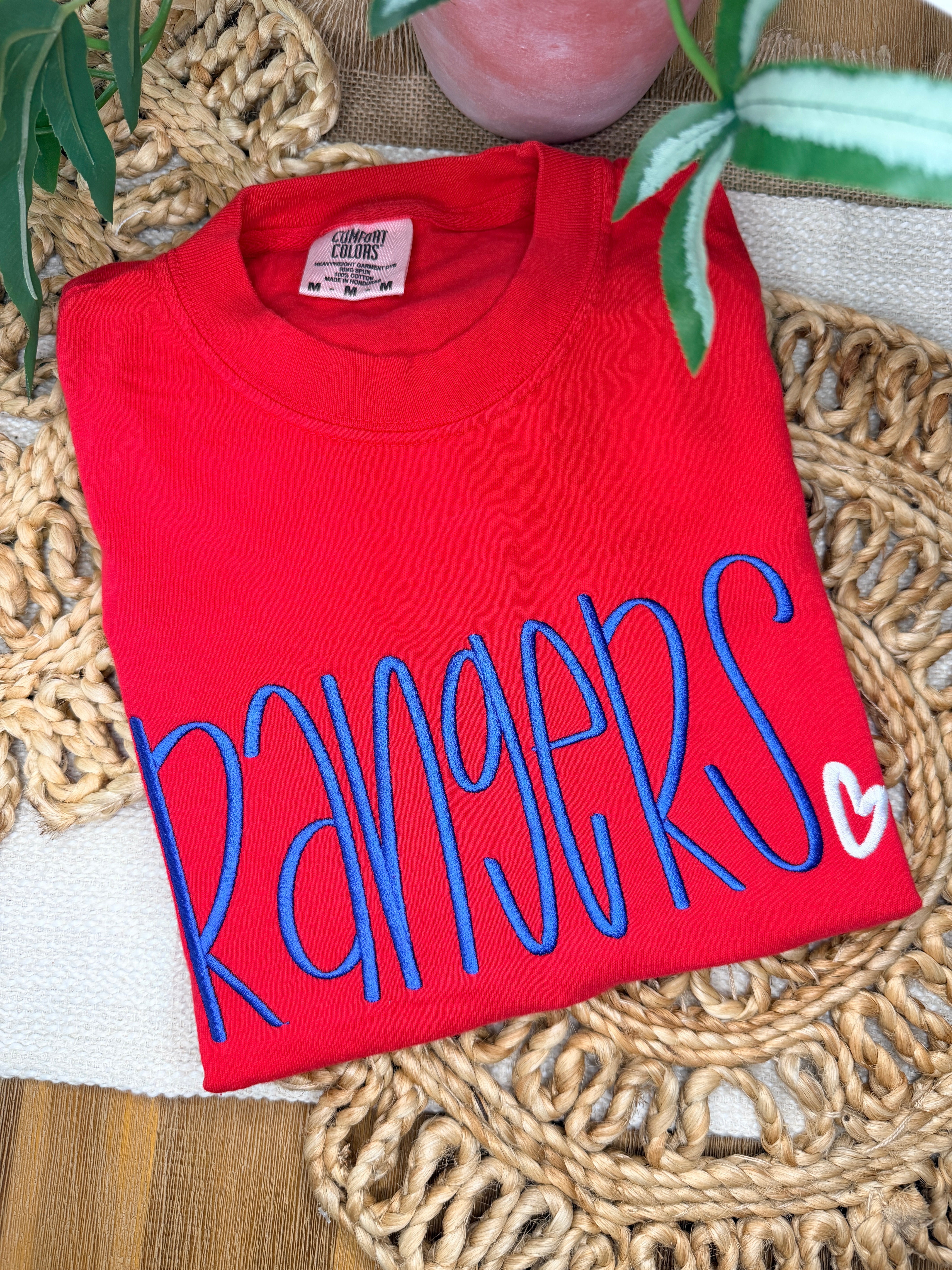Red Comfort Colors tee with large blue “Rangers” script embroidery and small white heart detail. Soft garment-dyed cotton with relaxed unisex fit and bold front design.