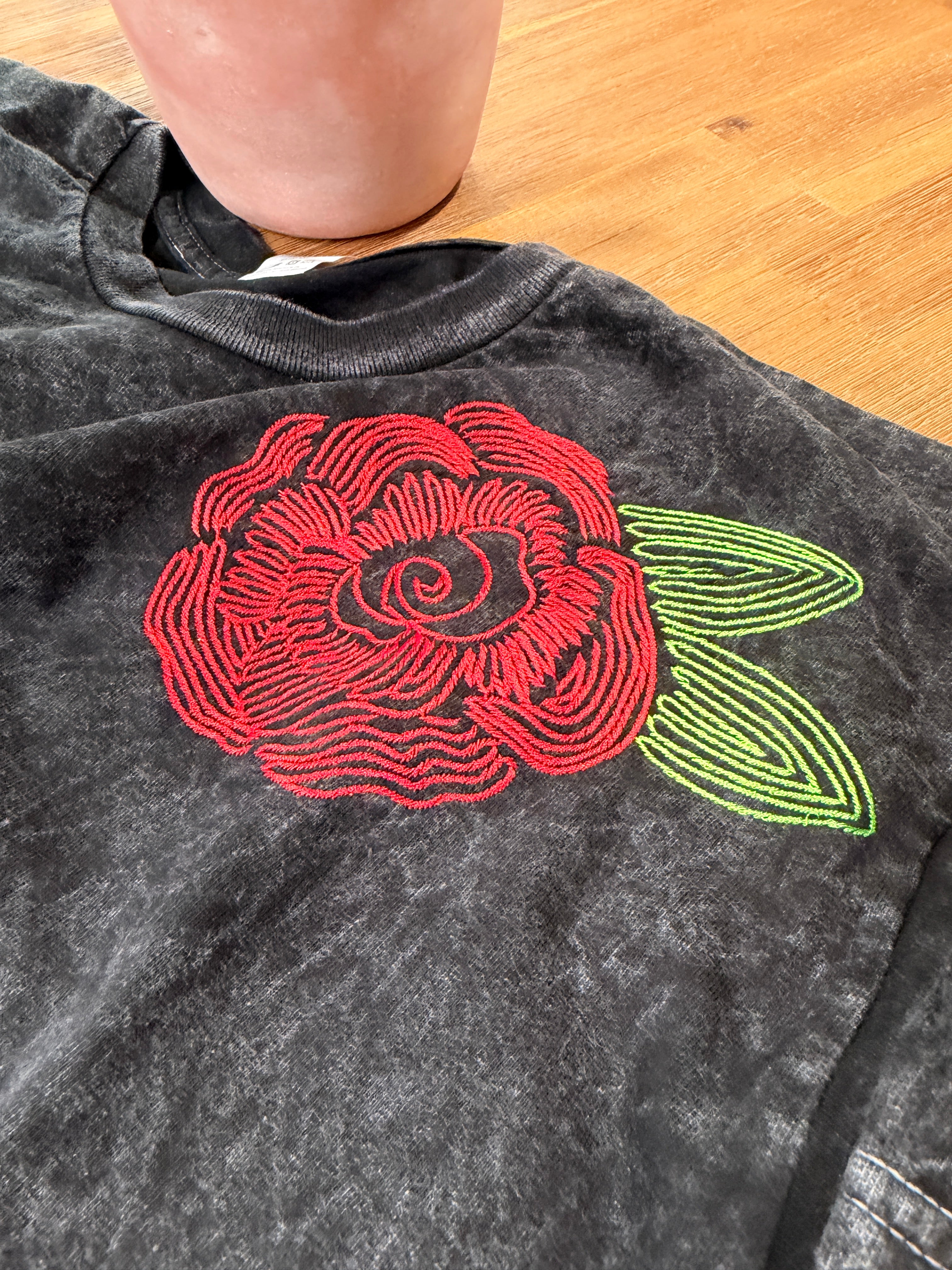Embroidered red rose with green leaves on a dark fabric background