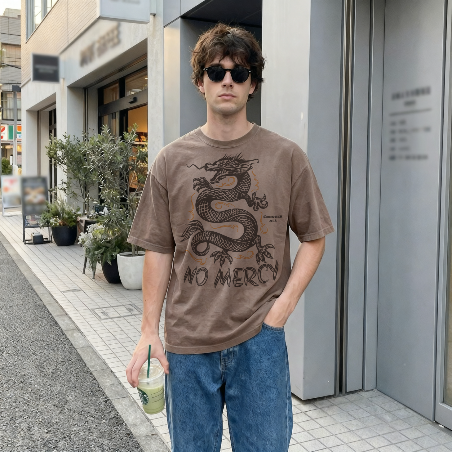 Man wearing a brown t-shirt with a dragon design and 'No Mercy' text, standing on a city street.