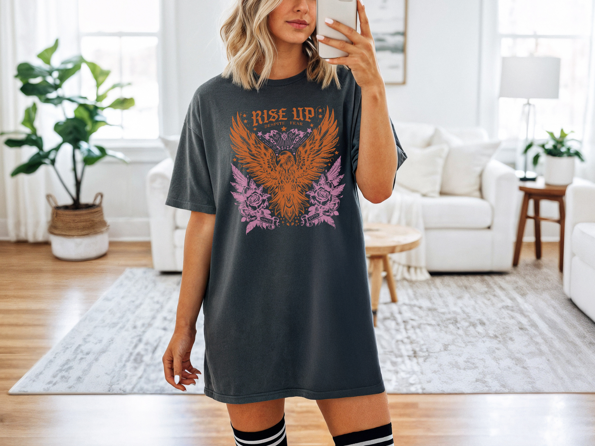 Woman taking a selfie wearing a dark gray t-shirt with an eagle design in a living room.