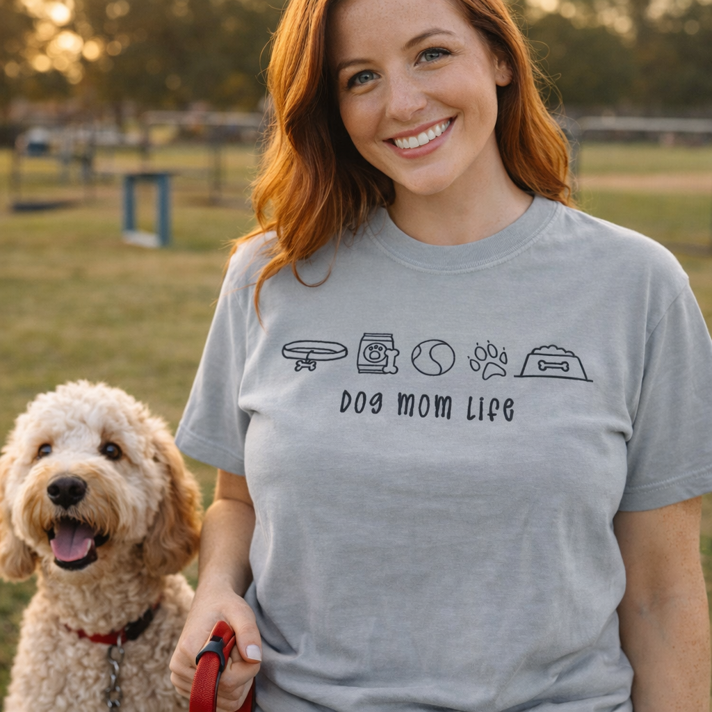 Woman wearing a 'Dog Mom Life' t-shirt with a dog at a park.