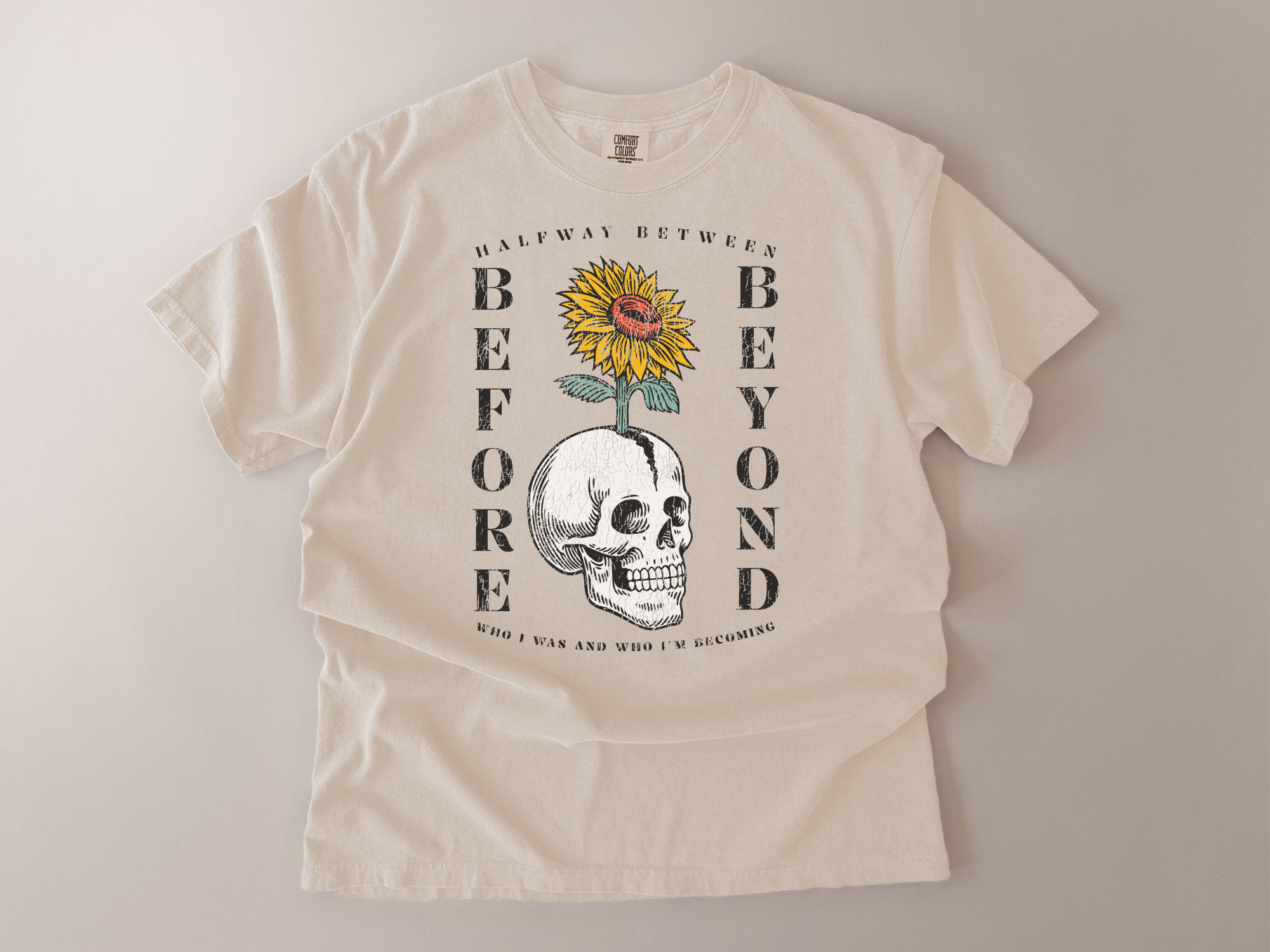 Beige t-shirt with skull and sunflower graphic and text on a plain background