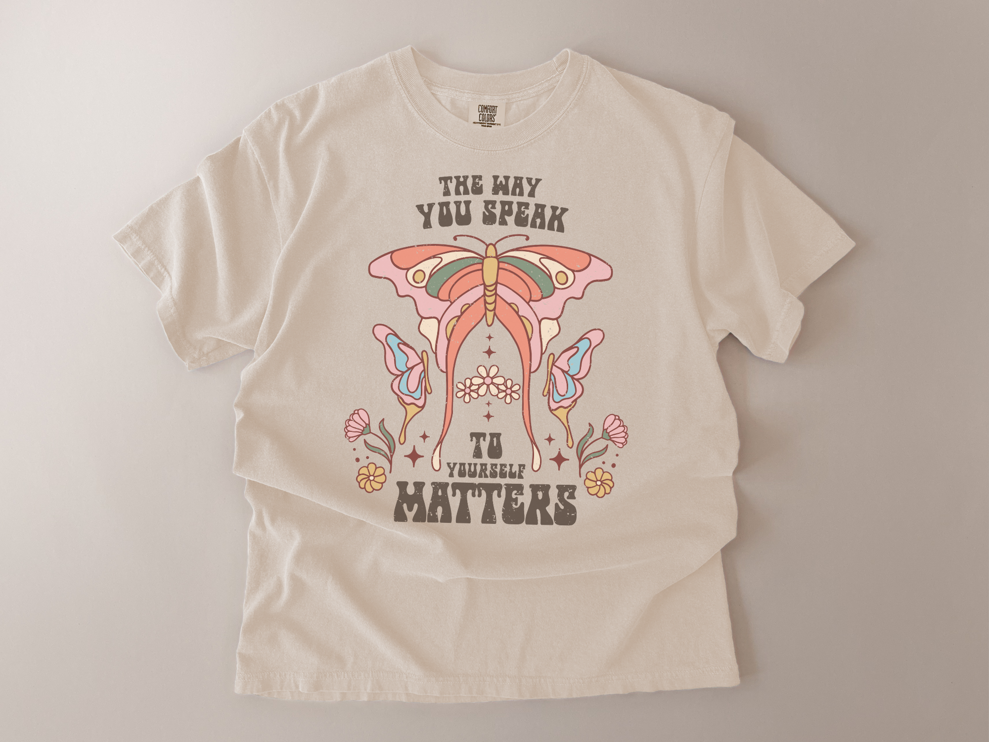 Beige t-shirt with colorful butterfly design and text on a plain background