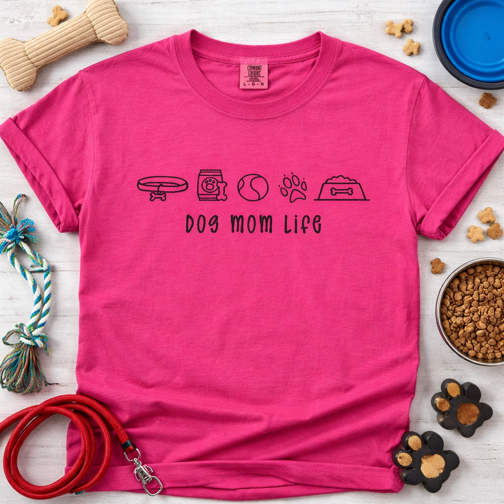 Pink t-shirt with 'Dog Mom Life' text and dog-themed accessories on a wooden surface.