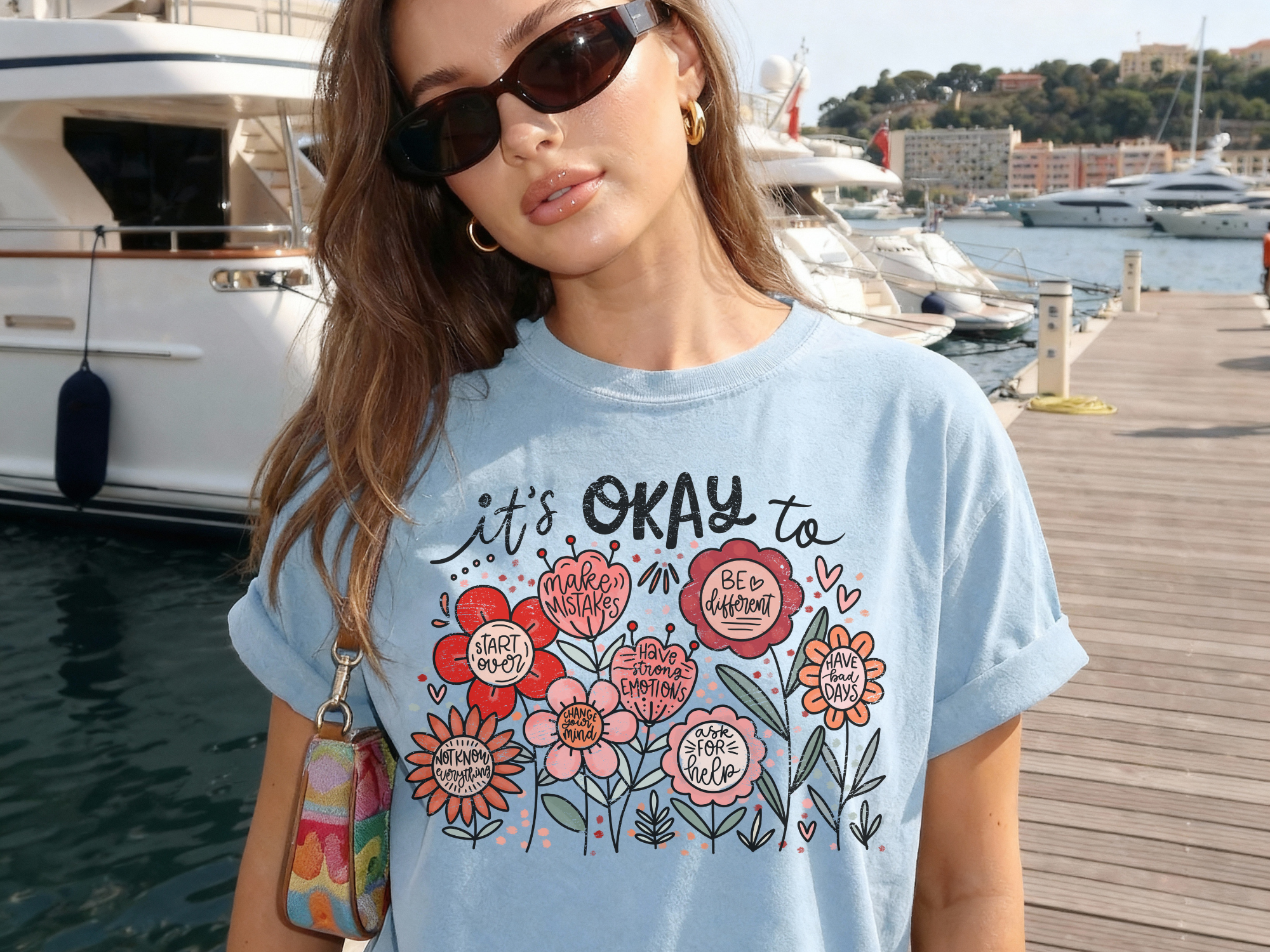 Woman wearing a light blue t-shirt with floral designs and text by a marina.