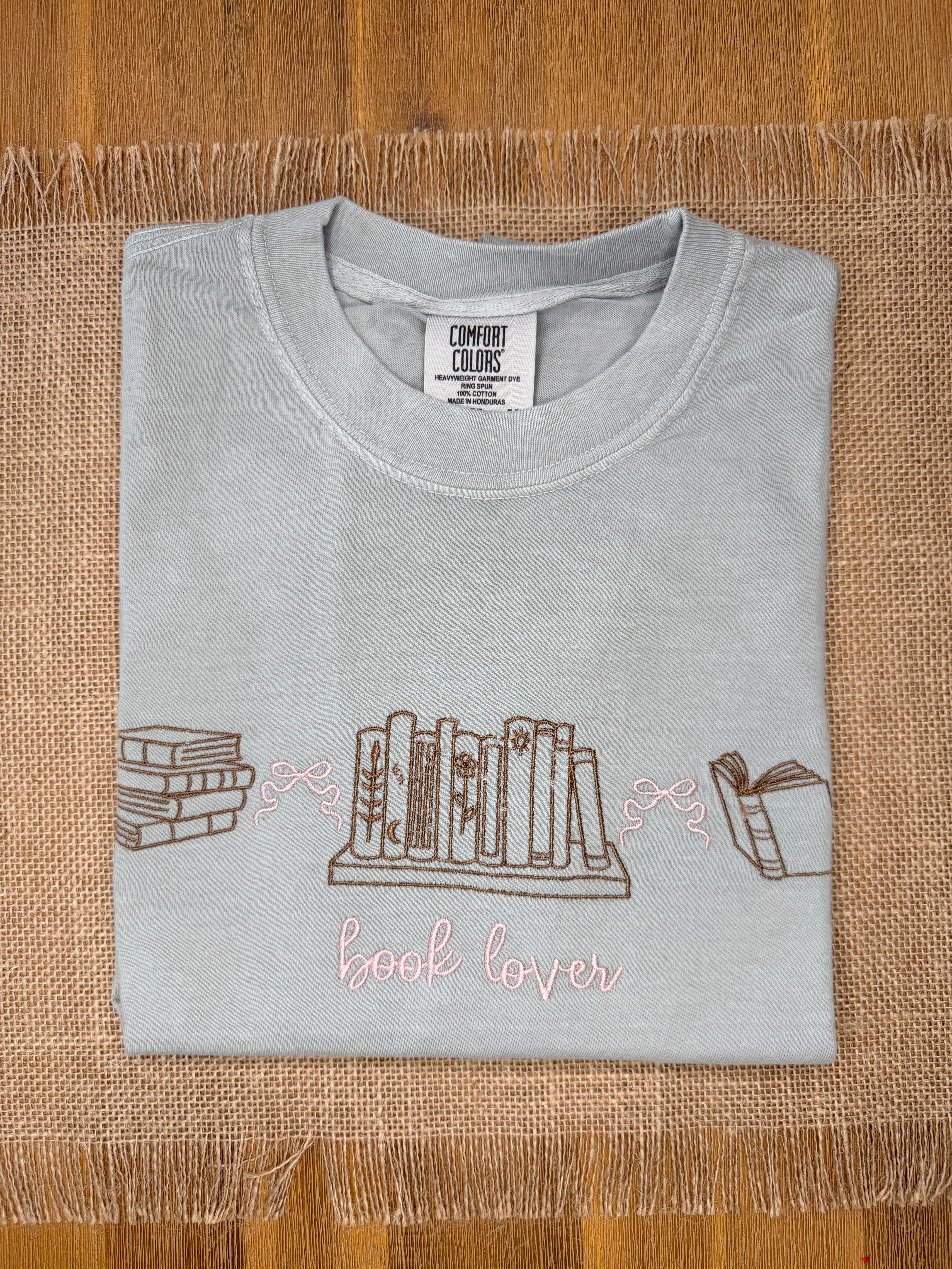Gray t-shirt with book-themed design on a woven mat