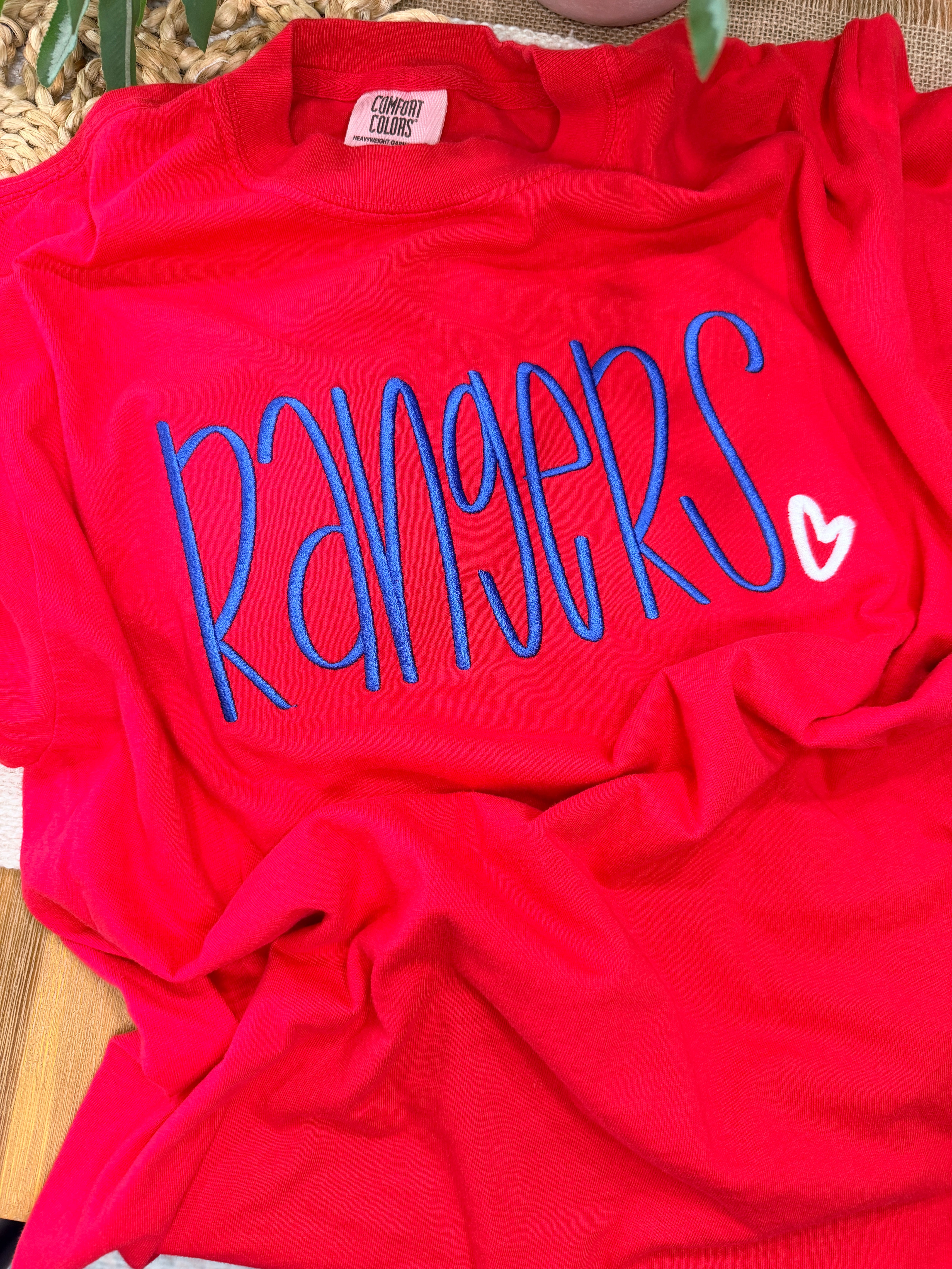 Red Comfort Colors tee with large blue “Rangers” script embroidery and small white heart detail. Soft garment-dyed cotton with relaxed unisex fit and bold front design.