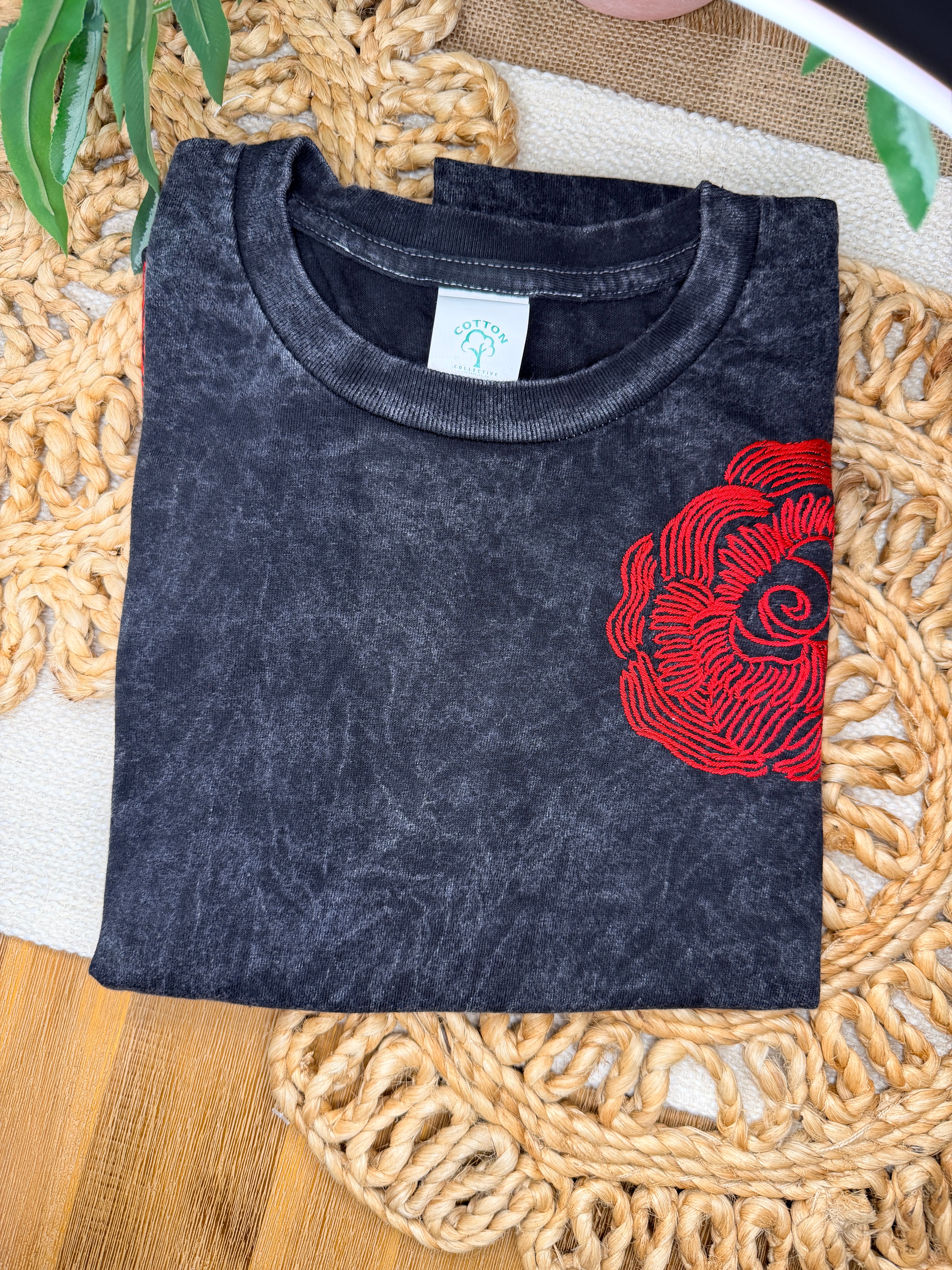 Black t-shirt with red floral design on a woven mat