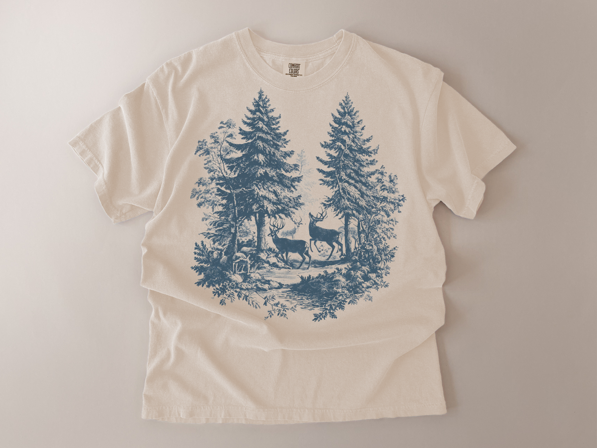 Beige t-shirt with blue forest design featuring deer on a light gray background