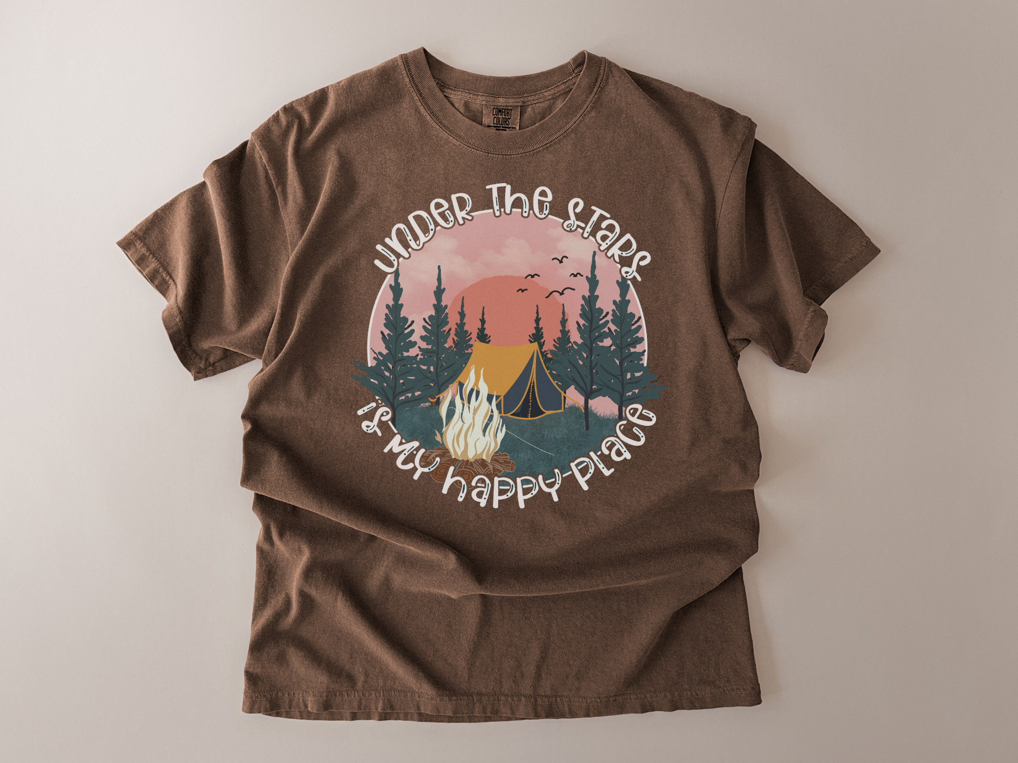 Brown t-shirt with a graphic design of a campsite and text on a beige background